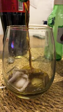 Pouring dark aromatic Fernet liqueur into a glass filled with ice cubes to prepare classic Argentine cocktail, night out, party
