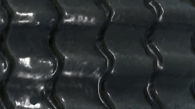 Glossy black ridged surface resembling wet rubber, tire treads, or synthetic plastic material. Features smooth curves and high contrast reflections.