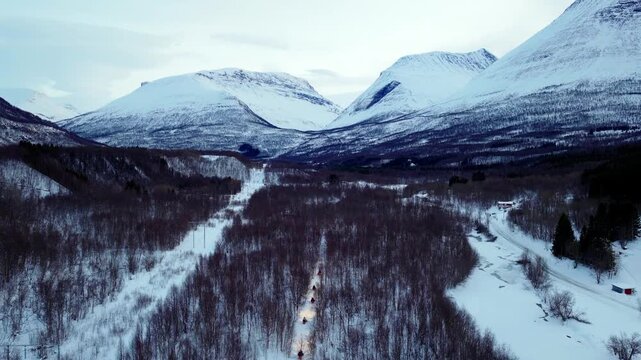 Aerial view of snowmobiles driving through a snow-covered forest with mountains in the background in Tromso, Troms, Norway.