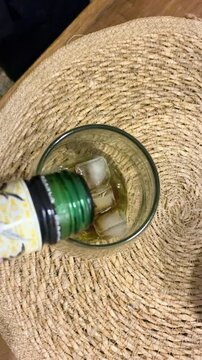 Pouring dark aromatic Fernet liqueur into a glass filled with ice cubes to prepare classic Argentine cocktail, night out
