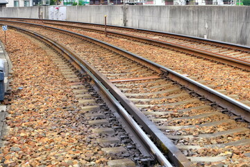 コンクリート壁沿いに続くバラスト軌道の線路とコンクリート枕木 © taka