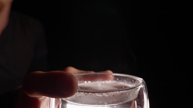 Person Holds a Steaming Glass of Hot Water Against a Dark Background, Showing Warmth, Hydration and Wellbeing