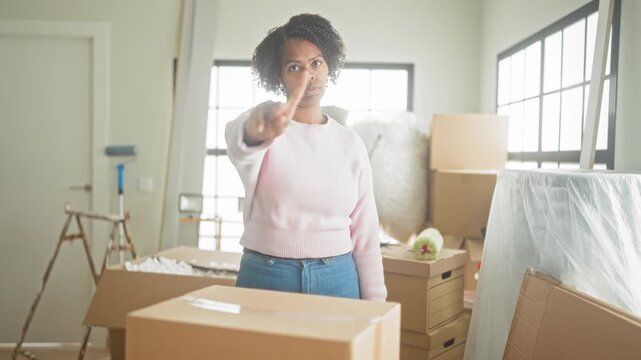 Woman points finger at stacked cardboard boxes and moving supplies in building as if signaling stop; determination.