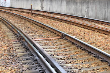 コンクリート壁沿いに続くバラスト軌道の線路とコンクリート枕木 © taka
