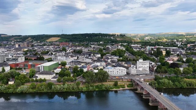 Zeitraffer (Timelapse)  Drohnenaufnahme von Trier mit der antiken R&ouml;merbr&uuml;cke &uuml;ber die Mosel, umgeben von Stadtarchitektur und gr&uuml;nen H&uuml;geln unter bew&ouml;lktem Himmel an einem Sommertag.