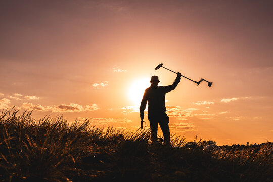 Silhouette of a Detectorist Lifting His Tool Skyward at Golden Hour