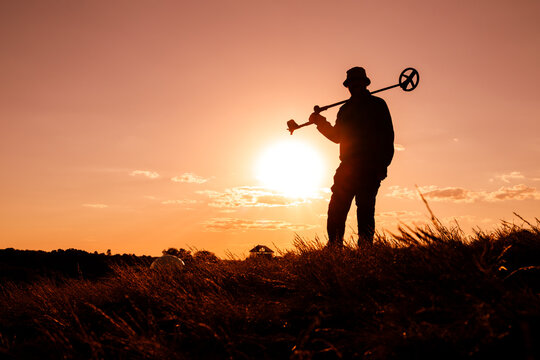 Man Carrying Metal Detector at Sunset, Fiery Orange Background
