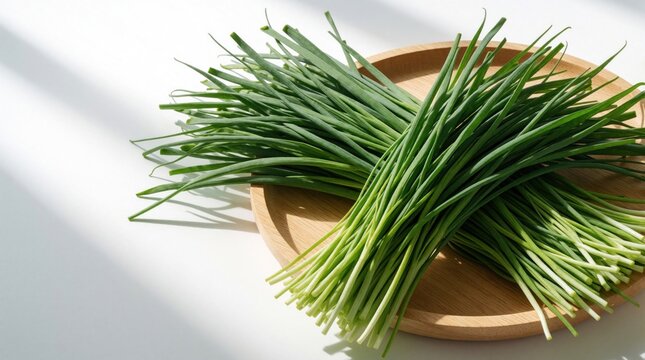 Fresh green Chinese chives, garlic chives lie on wooden plate. Raw organic vegetable stalks arranged on white background. Healthy herbal plant ingredients for cooking Asian food. Bunch of long green