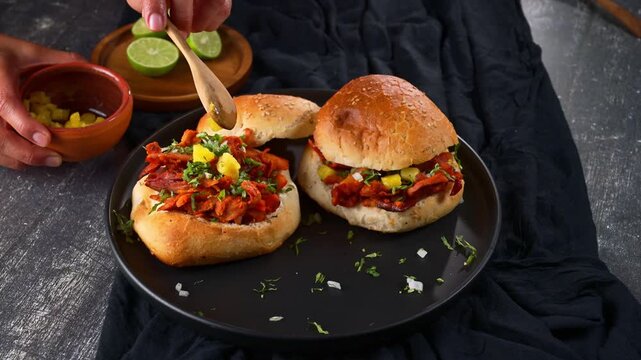 Top view of person garnishing homemade Mexican al pastor tortas with chopped pineapple on dark background