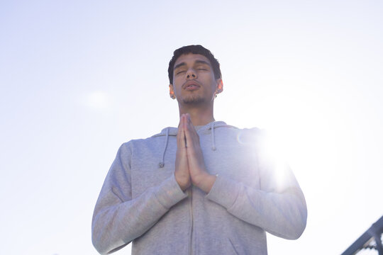 African American man standing hands pressing at chest on rooftop wearing gray hoodie lens flare