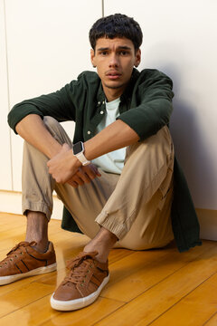 African American man sitting on hardwood floor leaning against white cabinetry, showing smartwatch