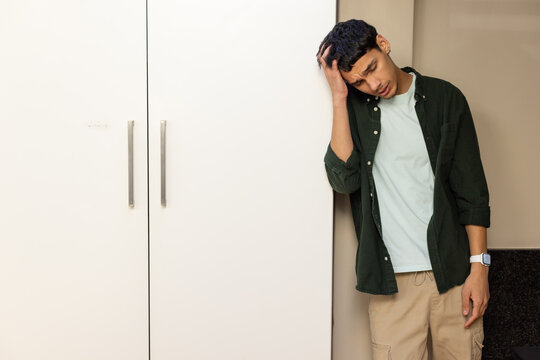 Man leaning against wardrobe at home with handles, pressing head, wearing smartwatch, copy space