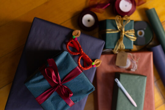 Teal gift tied with burgundy ribbon sitting atop dark plum box on wooden floor, with glasses