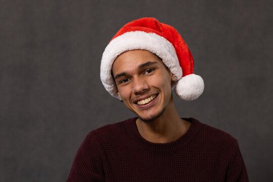Man smiling in portrait studio wearing red Santa hat, burgundy sweater, silver stud earrings