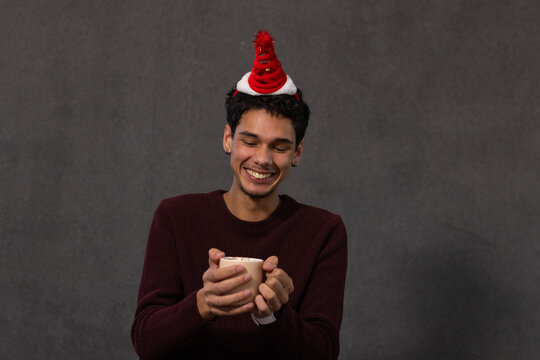 African American man sitting in studio holding ceramic mug wearing novelty spiral hat and sweater