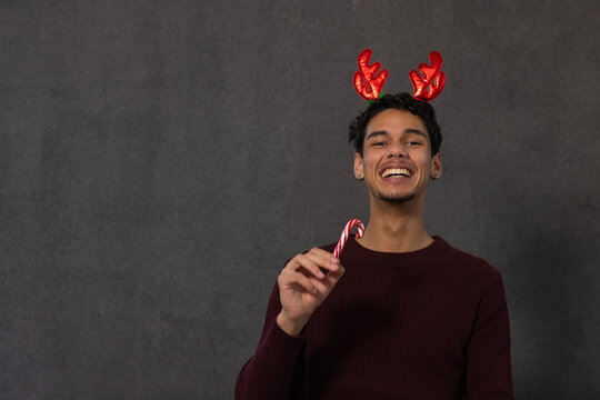 Man laughing while holding candy cane, wearing antlers and maroon sweater in studio, copy space
