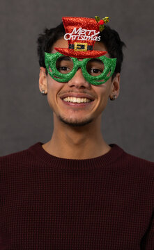 Adult African American man smiling at camera wearing glitter glasses, Merry hat, sweater in studio