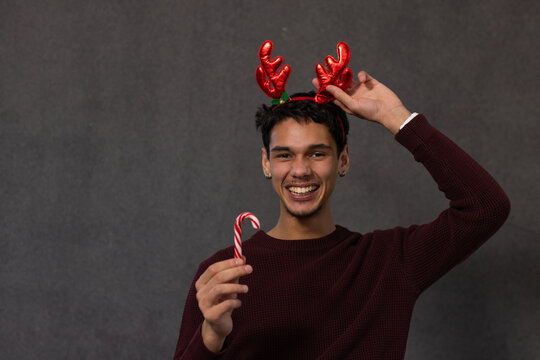 African American man smiling, adjusting red antlers and holding candy cane in maroon sweater studio