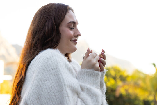 Female wearing oversized white sweater and hoop nose ring standing on terrace holding clear cup