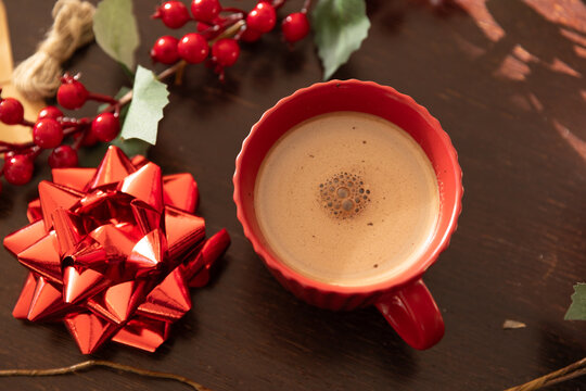 Red scalloped mug sitting on dark wooden table, showing crema and small bubbles with red bow