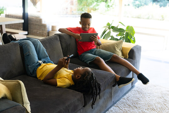 African youth males relaxing on dark gray sectional sofa at home, holding tablet and smartphone