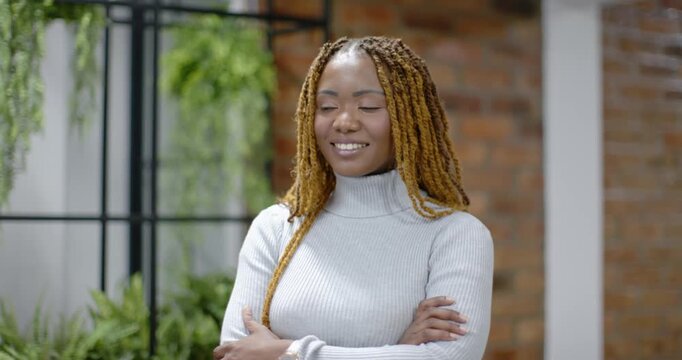 Mid-adult African woman standing arms crossed in studio, noticing someone off-frame near plant grid