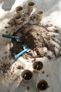 Potting soil mound is sitting on tarp with two trowels and peat pots under dappled sun