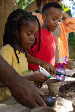African family gathering under tree at backyard table, preparing peat pots with soil, copy space