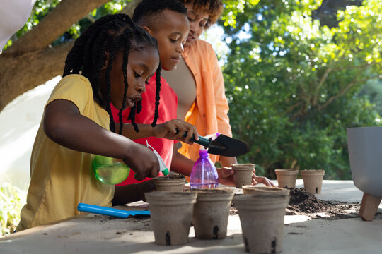 African American family wearing yellow and red shirts potting plants at garden table with peat pots