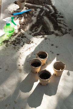 Four compost peat pots sitting on white sheet, soil pile spilling and spray bottle casting shadow