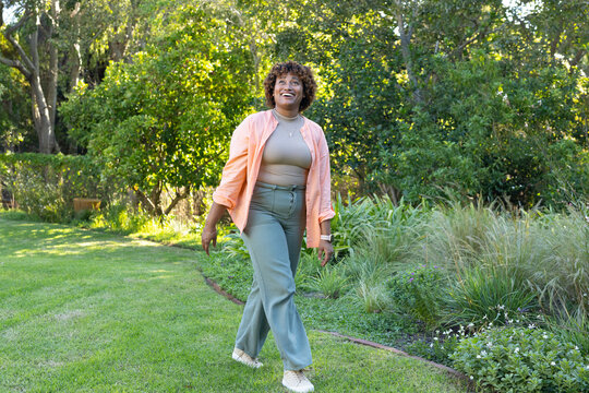 African American woman walking on curved lawn path in backyard wearing white sneakers and necklace