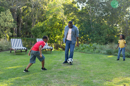 African American family playing soccer in backyard with soccer ball and striped lounge chairs