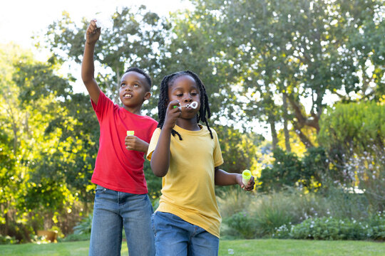 African children wearing red and yellow tees playing at park blowing bubbles with wands and bottles