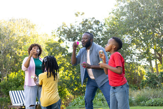 African American family blowing soap bubbles on green lawn in garden holding bubble wands
