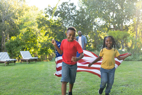 African American family watching kids running across lawn holding American flag by striped chairs