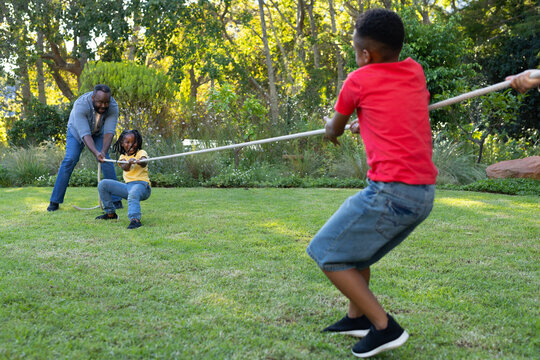 African family playing tug-of-war on grassy backyard lawn, children pulling long rope, copy space