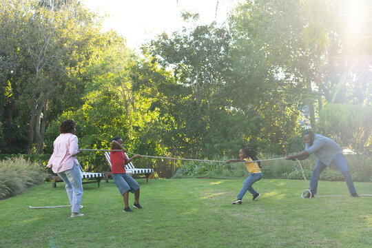 African American family pulling rope in yard for tug-of-war by bench with black-and-white cushions