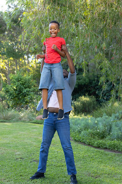 Father and son playing in garden lifting child to low-hanging branches, red T-shirt, denim shorts