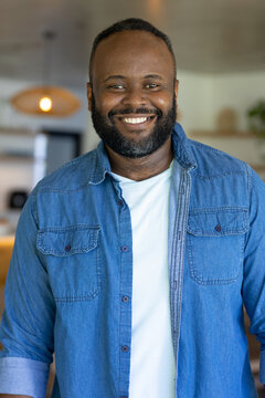 African American man smiling while standing in modern open-plan kitchen wearing blue denim shirt