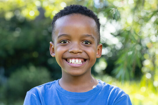 African male child smiling and looking at camera while wearing blue T-shirt in sunny garden