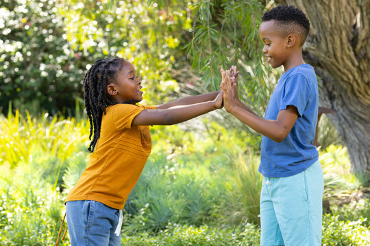 Two African youths playing hand-clapping on grassy lawn under dappled sunlight near tree trunk