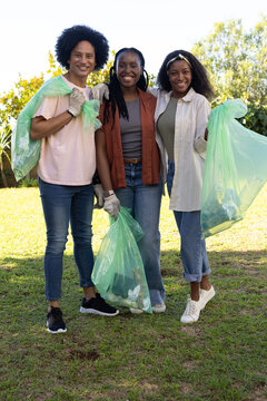 Volunteer group cleaning park wearing casual clothes and work gloves while holding green trash bags