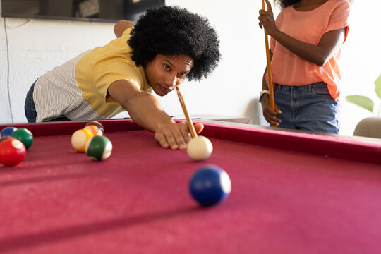 African American couple leaning at home pool table, woman wearing yellow lining up shot with cue