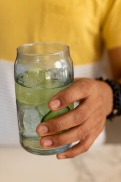African American male holding tumbler with ice cucumber at counter with droplets in yellow shirt