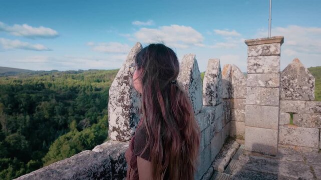 Contemplative young woman with long hair looking at the green valley from the top of the medieval fortress of Pambre Castle, in Galicia, Spain, enjoying a peaceful and serene moment