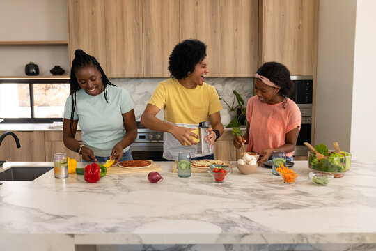African American friends chopping bell pepper, grating over pizza bases on marble kitchen island