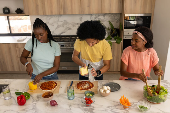 African American friends preparing pizzas and tossing salad on marble island with fresh vegetables