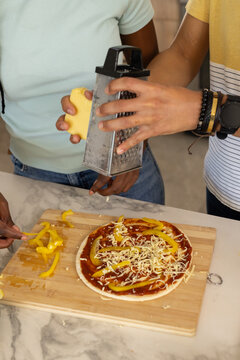Two friends in blue and striped tops grating cheese with box grater assembling pizza on board
