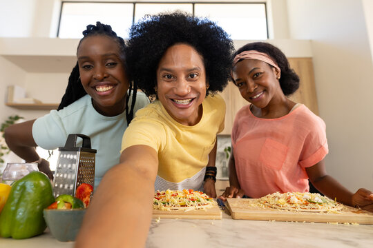 African American friends cooking and taking selfie in kitchen with cutting boards, grater, peppers