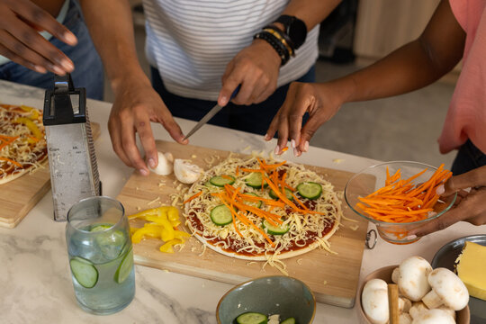 African American friends wearing casual wear assembling pizzas on marble counter with grater knife